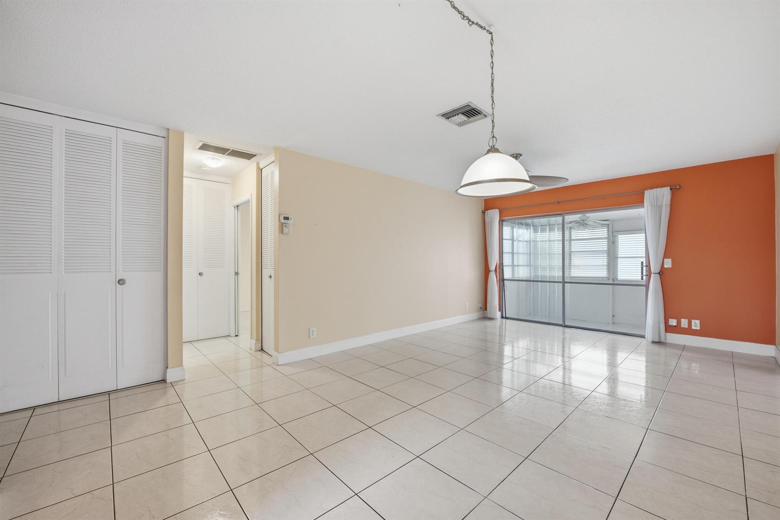 An empty room with beige walls, an orange accent wall, tile floors, and sliding doors — 2789 Ashley Drive W # C, West Palm Beach FL 33415, WEST PALM BEACH, FL