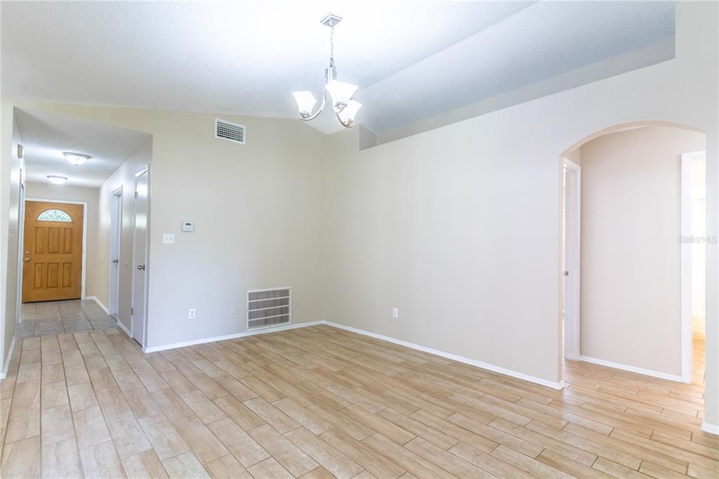An empty room with light wood-look tile flooring, a chandelier, and an arched doorway — 9624 TETLEY COURT, ORLANDO, FL