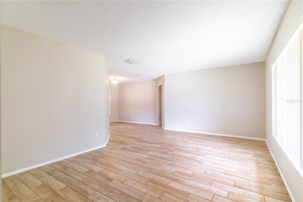 An empty living area features light-colored walls, wood-look tile flooring, and vertical window blinds — 9624 TETLEY COURT, ORLANDO, FL