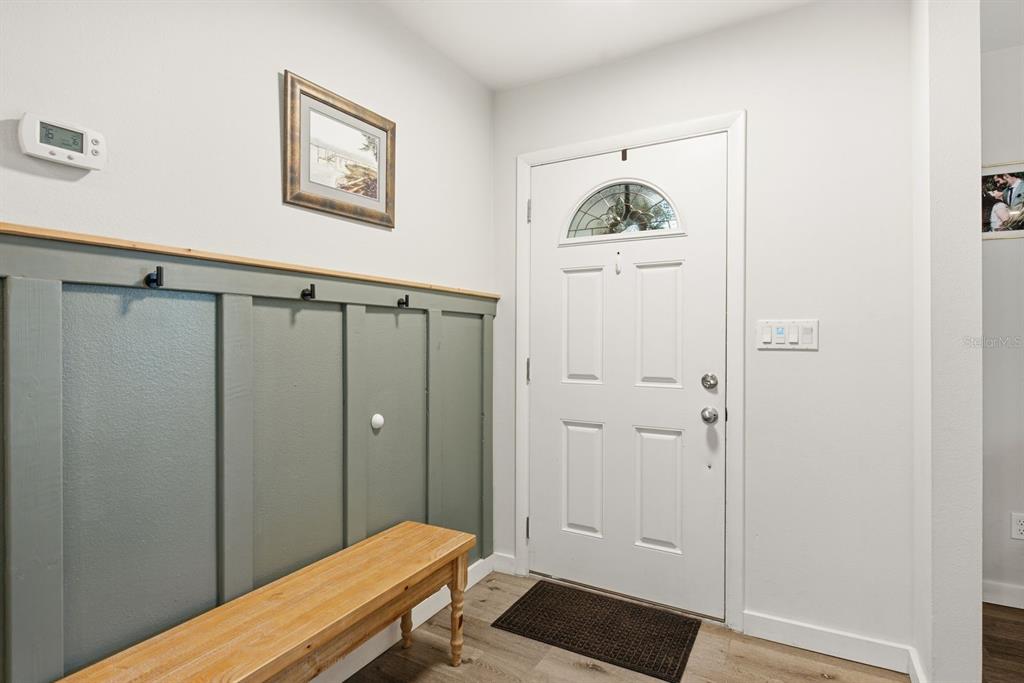 An entryway features a wooden bench, sage green board and batten wainscoting, and a white door — 3229 SPANISH MOSS LANE, PALM HARBOR, FL