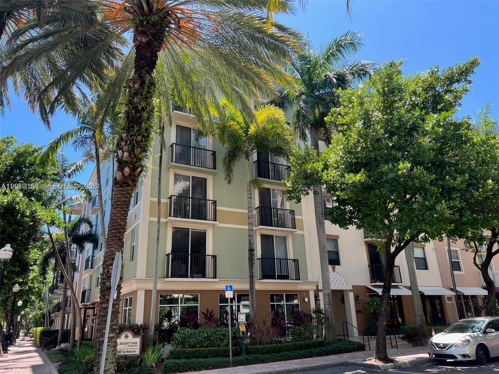 A multi-story apartment building with balconies and palm trees sits along a sidewalk — 1900 Van Buren St # 111B, Hollywood FL 33020, HOLLYWOOD, FL