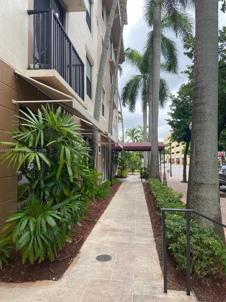 A paved walkway runs alongside a multi-story building with palm trees and landscaping — 1900 Van Buren St # 111B, Hollywood FL 33020, HOLLYWOOD, FL