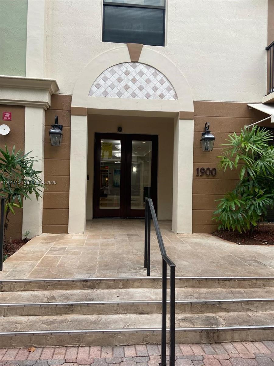 The exterior entrance of a building features stone steps, a glass double door, and sconces — 1900 Van Buren St # 111B, Hollywood FL 33020, HOLLYWOOD, FL