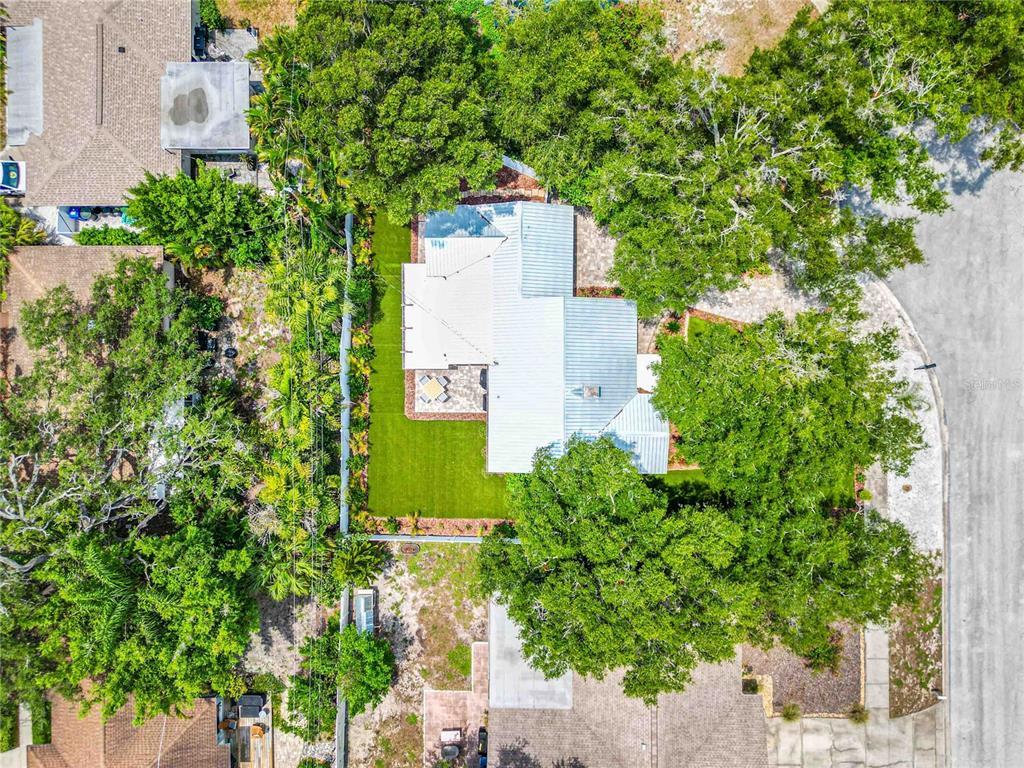 An aerial view shows a house with a metal roof surrounded by trees and landscaping — 131 VALENCIA DRIVE, DUNEDIN, FL