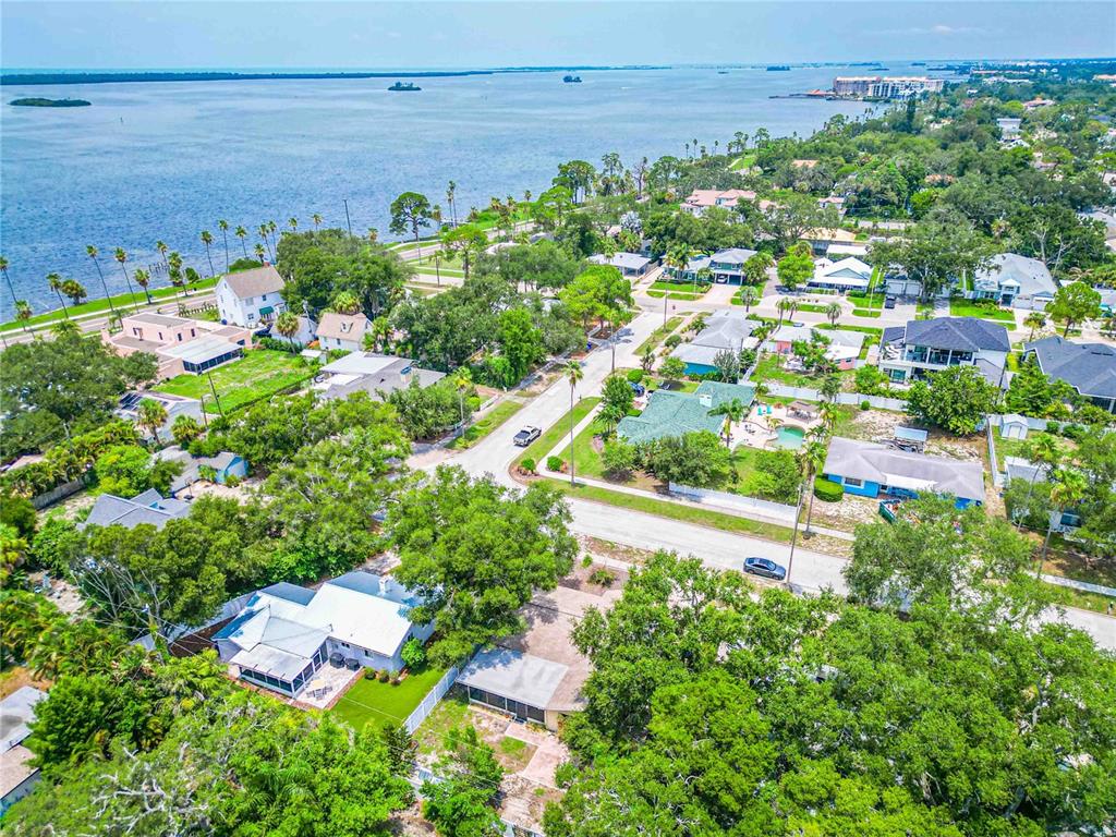An aerial view shows a residential neighborhood with houses, lush trees, and a nearby bay — 131 VALENCIA DRIVE, DUNEDIN, FL