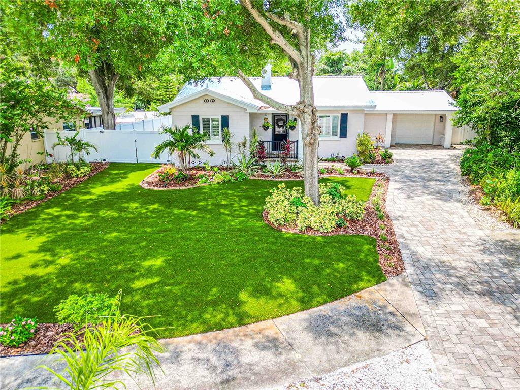 A single-story house with a white roof, brick driveway, and a manicured artificial turf lawn — 131 VALENCIA DRIVE, DUNEDIN, FL