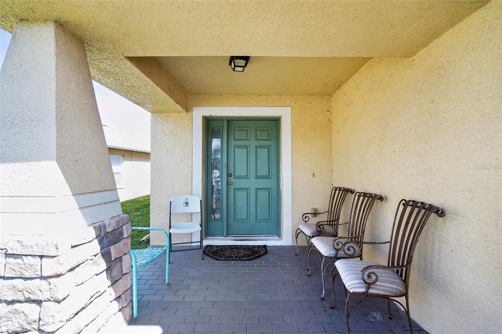 A covered front porch features a teal door, tiled flooring, and several outdoor chairs — 31417 TRIBOROUGH DRIVE, WESLEY CHAPEL, FL