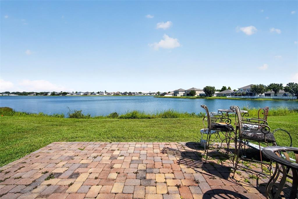A paved patio overlooks a large lake with houses visible along the distant shoreline — 31417 TRIBOROUGH DRIVE, WESLEY CHAPEL, FL