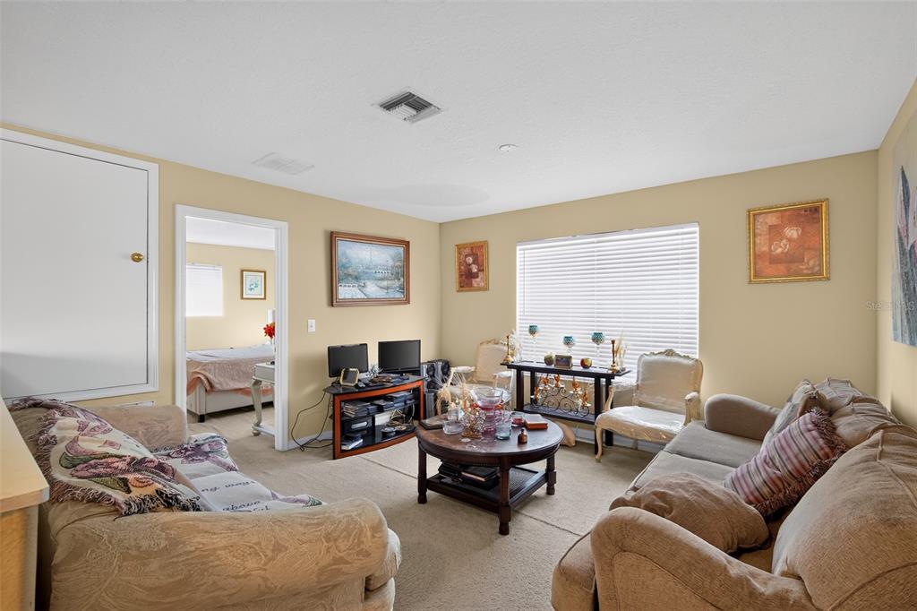 A living room with beige carpet, tan walls, two sofas, a coffee table, and a doorway — 31417 TRIBOROUGH DRIVE, WESLEY CHAPEL, FL