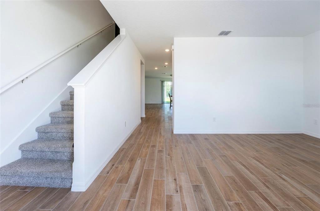 A carpeted staircase sits beside a wood-look tiled floor in a bright, open-concept living area — 4551 PICKEREL WEED WAY, ST CLOUD, FL