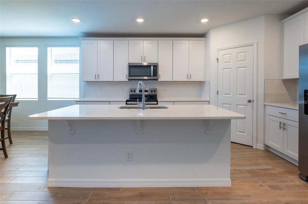 A kitchen features white cabinets, a large island with a sink, and light wood flooring — 4551 PICKEREL WEED WAY, ST CLOUD, FL