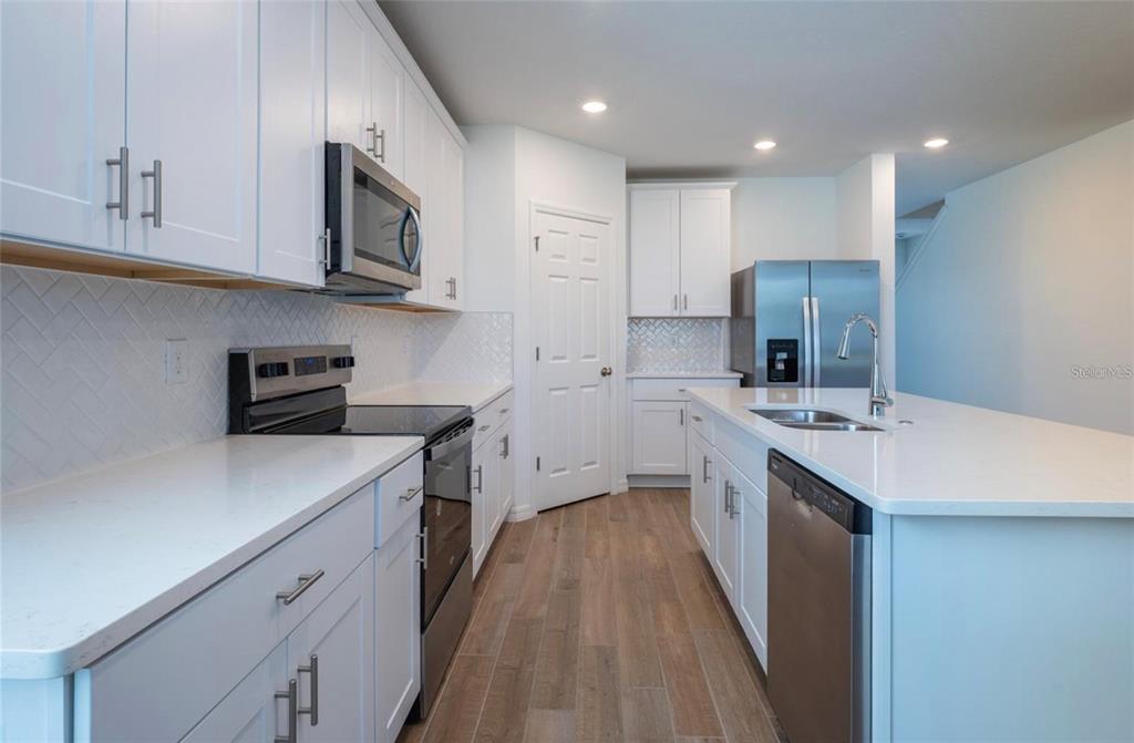 A modern kitchen features white cabinets, stainless steel appliances, quartz countertops, and wood-look tile flooring — 4551 PICKEREL WEED WAY, ST CLOUD, FL