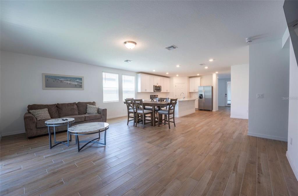 An open-concept living and dining area features light wood-look tile flooring and white kitchen cabinets — 4551 PICKEREL WEED WAY, ST CLOUD, FL