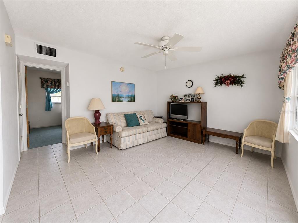 A living room with tile flooring, a striped sofa, two chairs, and a media console — 250 ROSERY ROAD NW UNIT 328, LARGO, FL