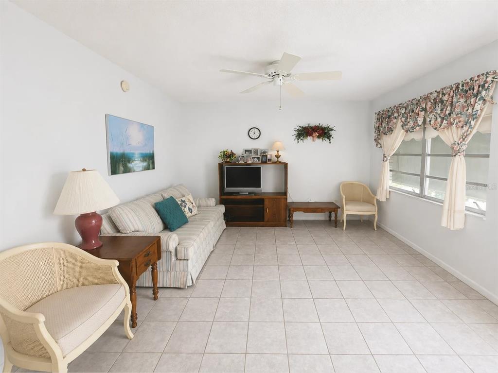 A living room with tile flooring, a striped sofa, two chairs, and a television console — 250 ROSERY ROAD NW UNIT 328, LARGO, FL