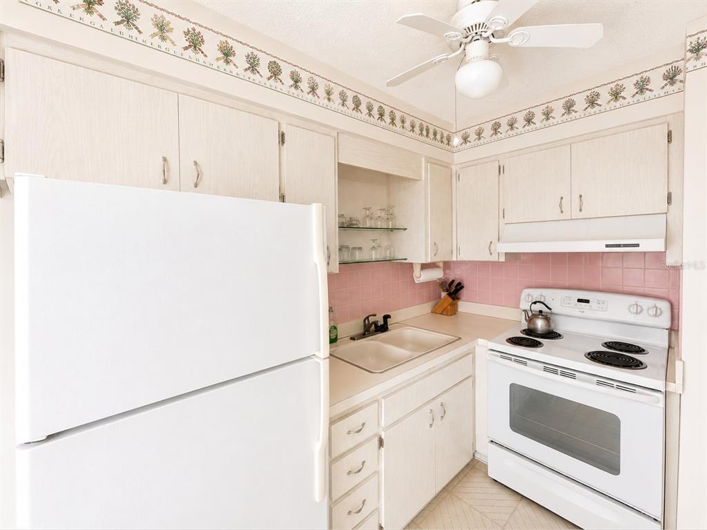 A kitchen features light wood cabinets, a white refrigerator, a white stove, and pink tile — 250 ROSERY ROAD NW UNIT 328, LARGO, FL