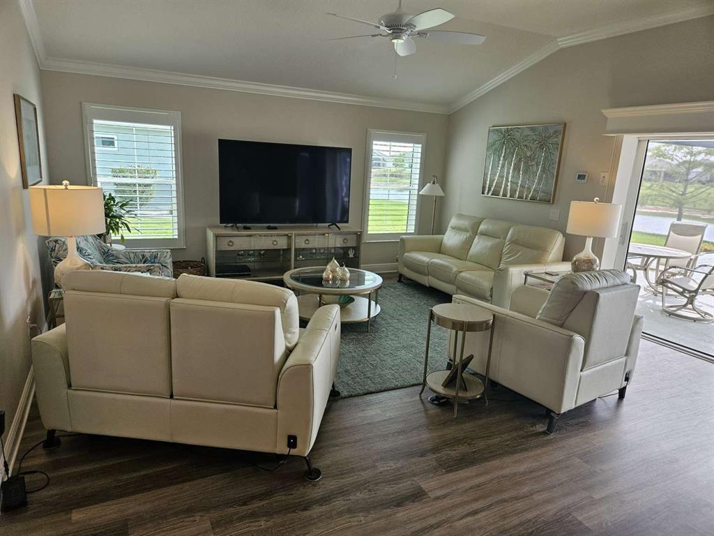 A living room features light-colored leather furniture, a television console, and a view of water — 7602 FRANK DIPIETRO DRIVE, THE VILLAGES, FL