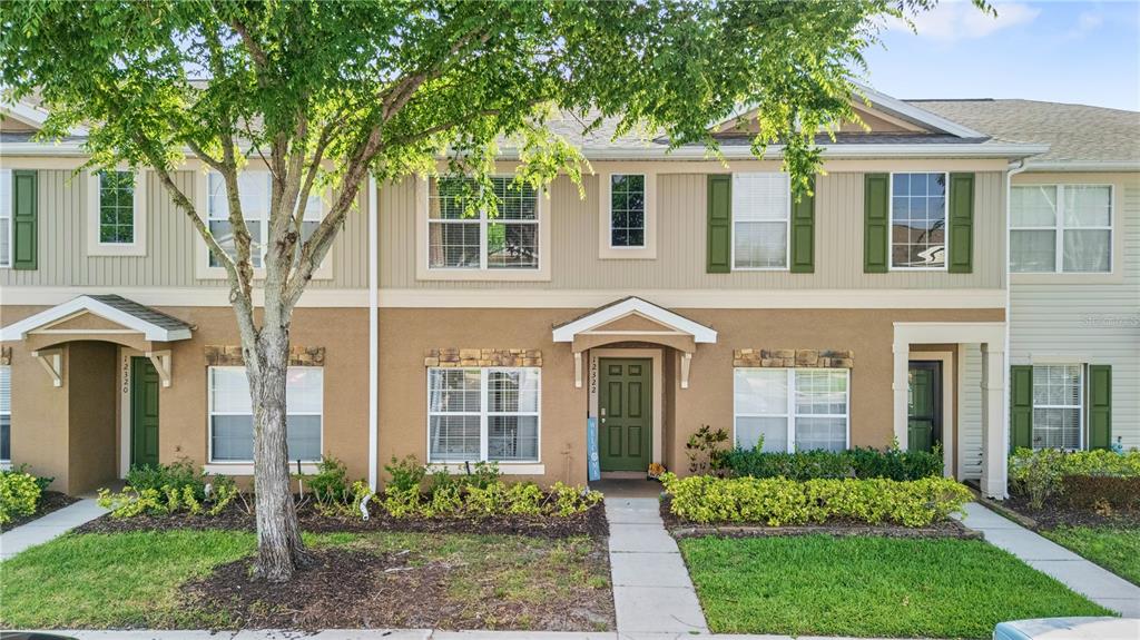 A two-story townhouse exterior features tan stucco, beige siding, green shutters, and small front gardens — 12322 FOXMOOR PEAK DRIVE, RIVERVIEW, FL