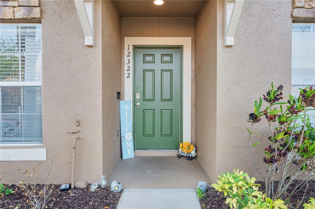 A green front door with a welcome sign sits under a covered entryway — 12322 FOXMOOR PEAK DRIVE, RIVERVIEW, FL
