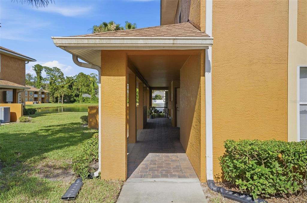 A covered walkway with brick pavers leads to an apartment entrance beside a grassy pond — 4600 E MOODY BOULEVARD UNIT 1P, BUNNELL, FL