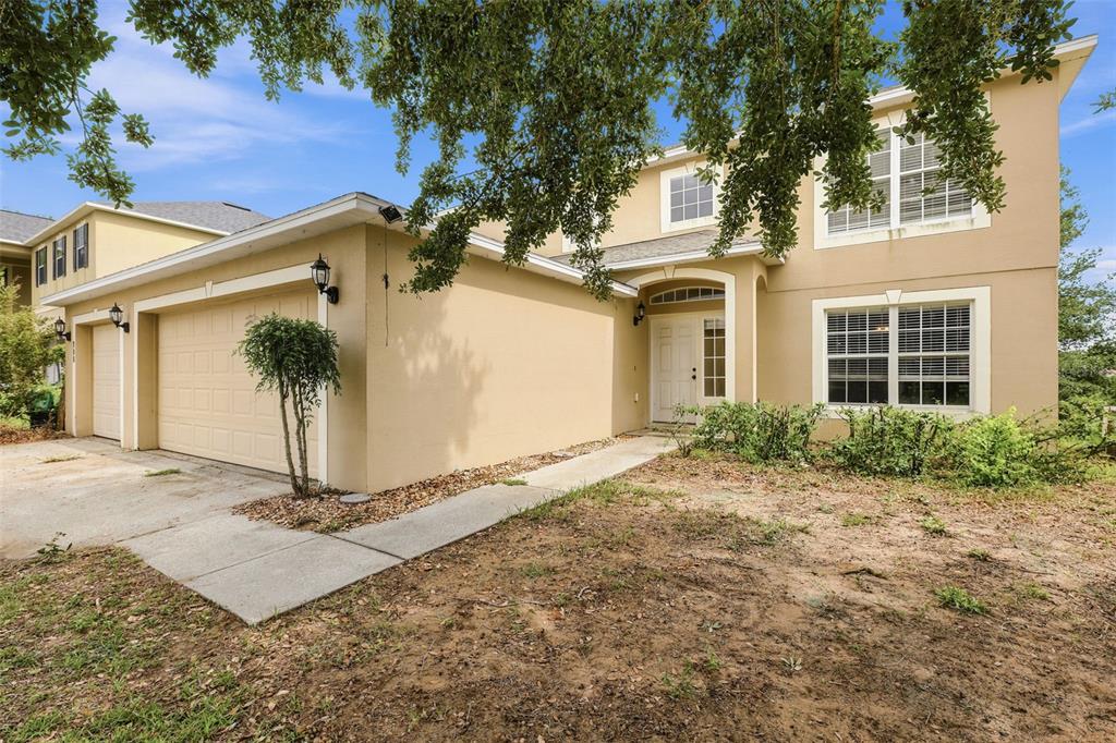 A two-story tan stucco house with a two-car garage and a front walkway — 800 MARIETTA LANE, EUSTIS, FL