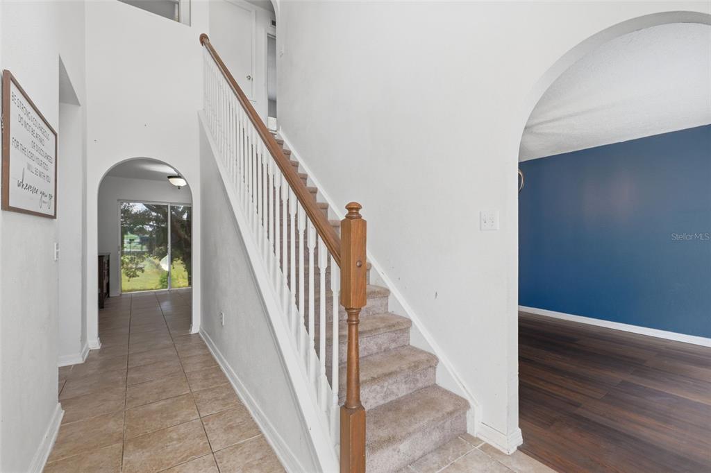 A carpeted staircase with a wooden railing sits between a tiled hallway and a room — 800 MARIETTA LANE, EUSTIS, FL
