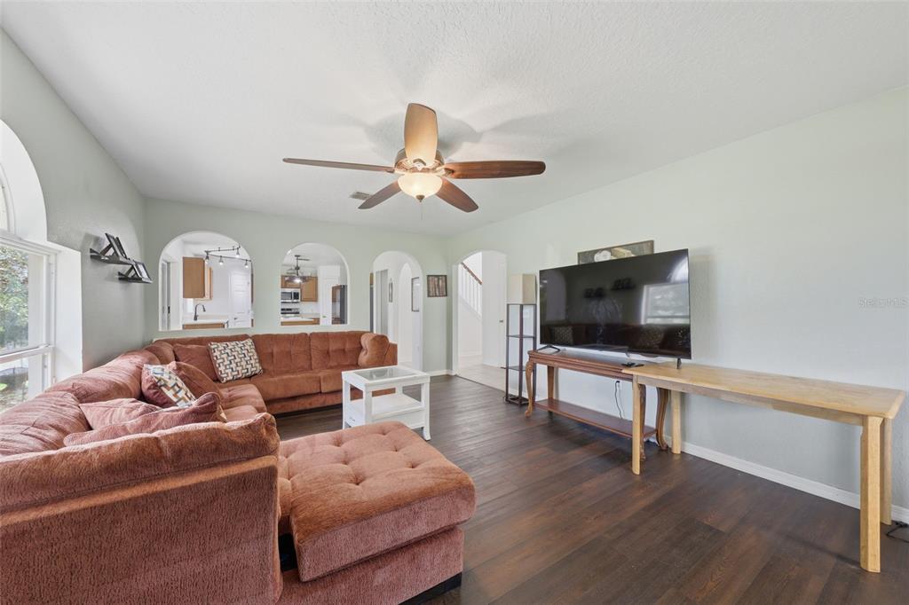 A living room features a large brown sectional sofa, dark wood flooring, and arched wall openings — 800 MARIETTA LANE, EUSTIS, FL