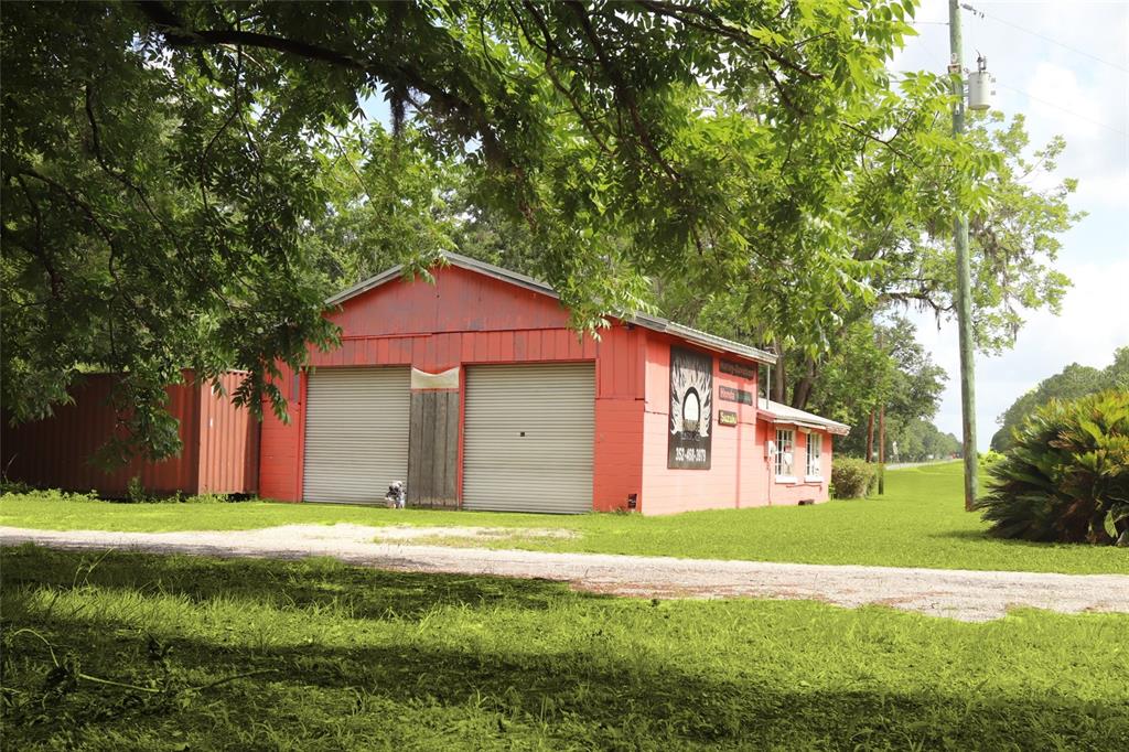 A red metal-sided workshop building with two roll-up garage doors sits on a grassy lot — 7220 NE US HIGHWAY 301, HAWTHORNE, FL