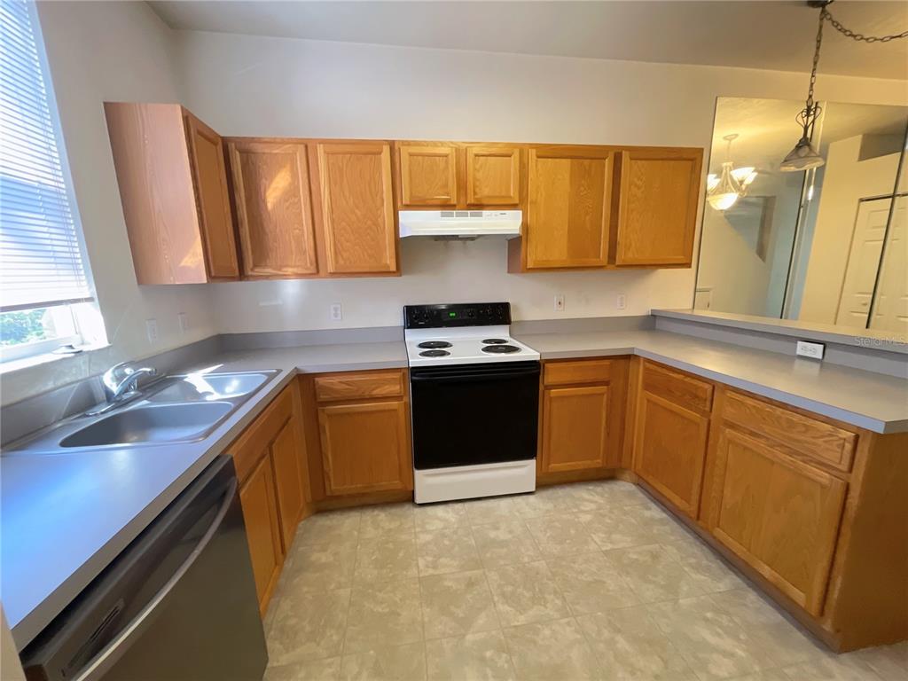 A kitchen features oak cabinets, gray laminate countertops, a white stove, and a double sink — 3930 SW 20TH AVENUE UNIT 1902, GAINESVILLE, FL