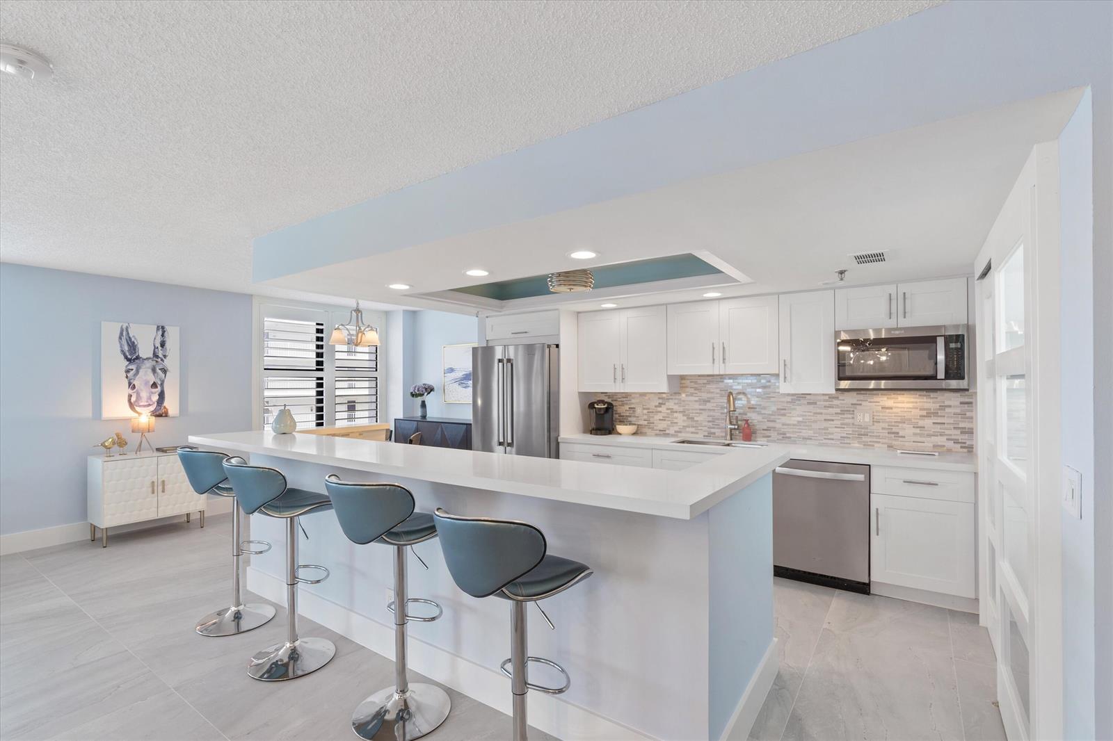 A modern kitchen features white cabinetry, stainless steel appliances, and a breakfast bar with stools — 3115 S Ocean Boulevard # 302, Highland Beach FL 33487, HIGHLAND BEACH, FL