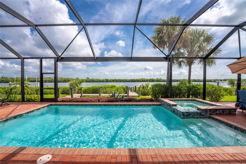 A screened-in pool and hot tub overlook a river with a wooden dock and palm trees — 15248 SPANISH POINT DRIVE, PORT CHARLOTTE, FL
