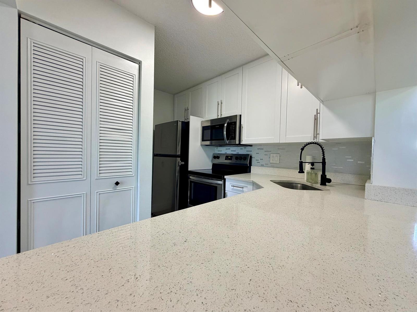 A kitchen features white cabinets, quartz countertops, stainless steel appliances, and a black faucet — 616 Sea Pine Way # C3, FL 33415, FL