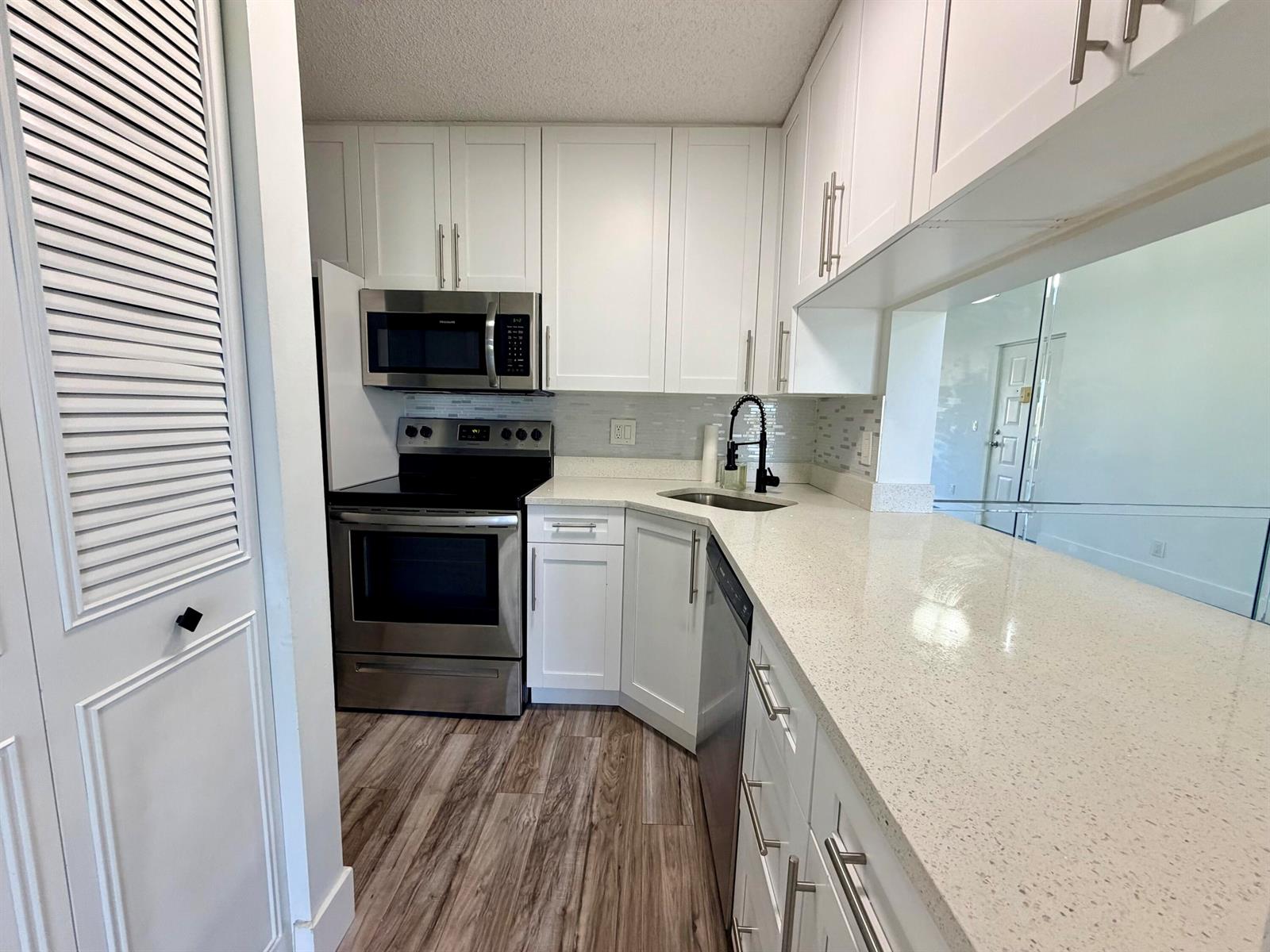 A kitchen features white cabinets, stainless steel appliances, and light-colored countertops with a breakfast bar — 616 Sea Pine Way # C3, FL 33415, FL