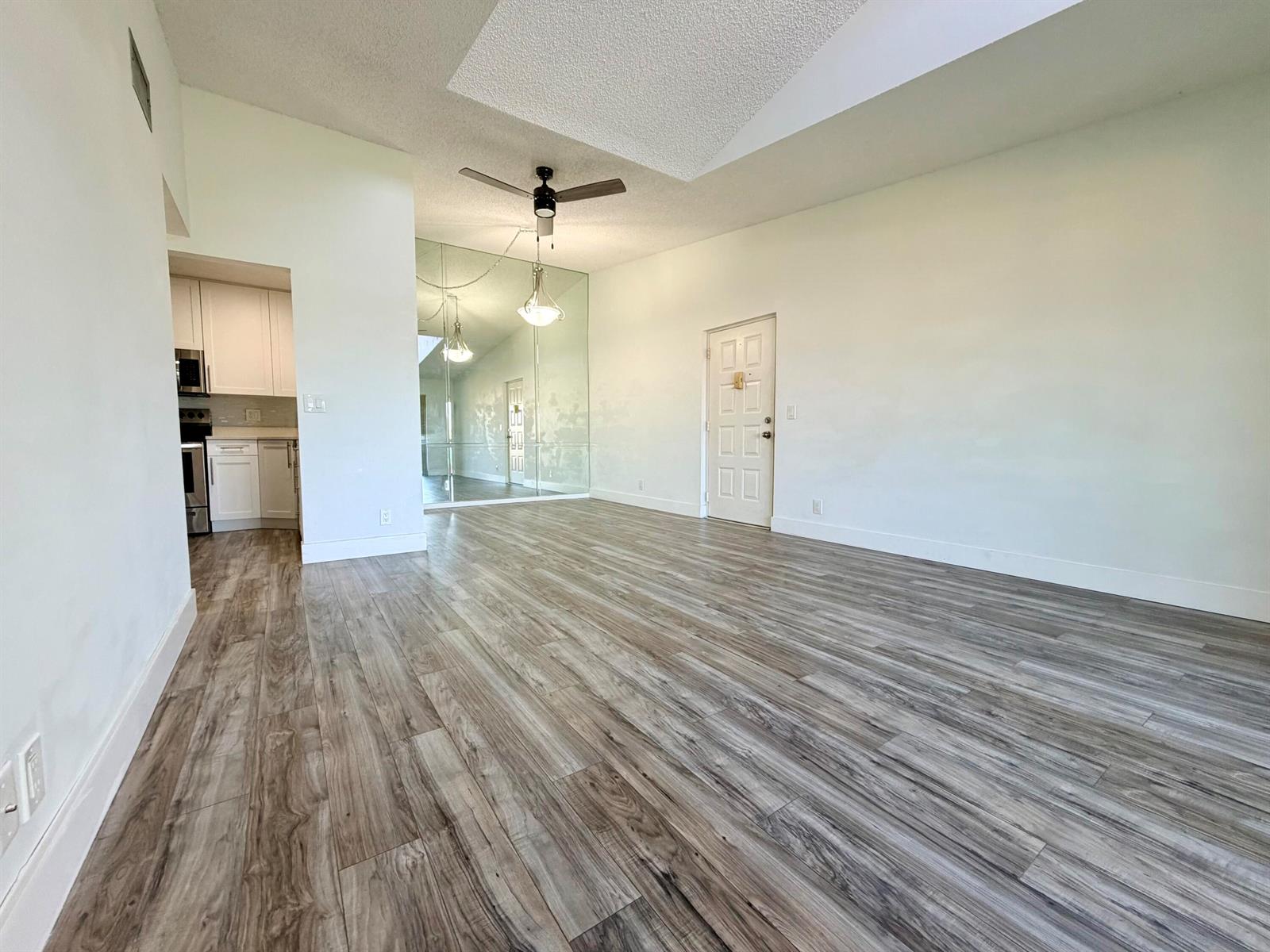 An empty living room features wood-look flooring, a mirrored wall, and a vaulted ceiling — 616 Sea Pine Way # C3, FL 33415, FL