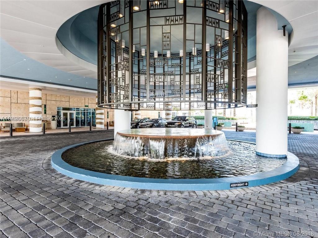 A circular fountain sits beneath a decorative metal structure at a building entrance — 6799 Collins Ave # 301, Miami Beach FL 33141, MIAMI BEACH, FL