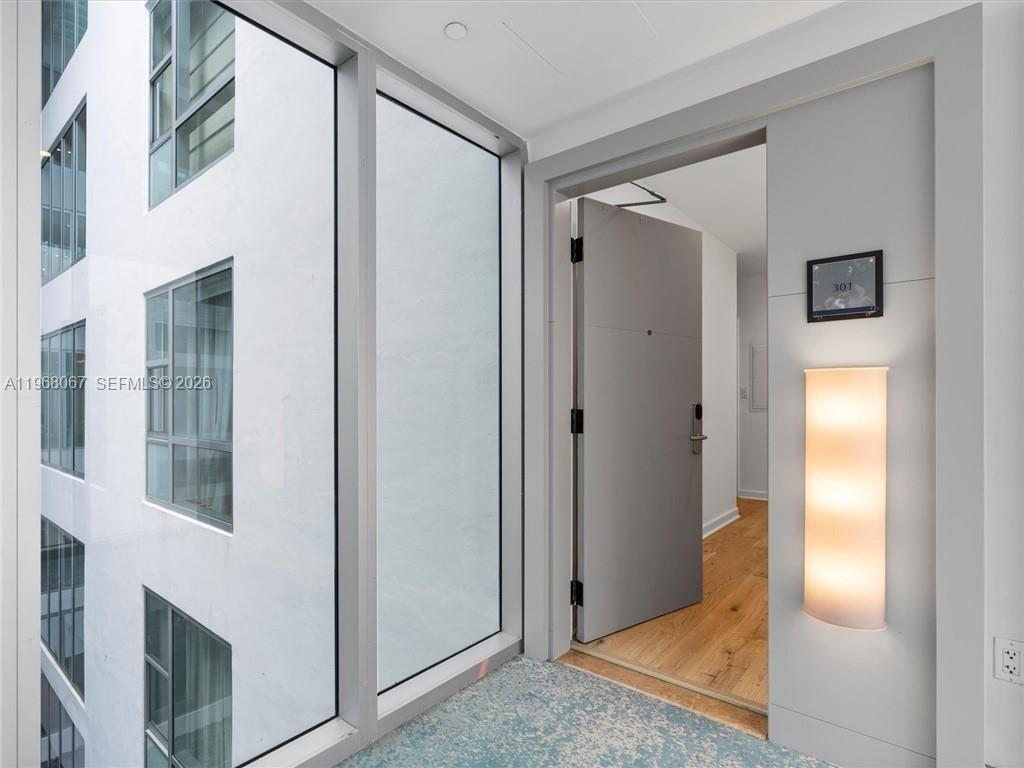 A modern apartment entrance features a gray door, wood flooring, and a large glass window — 6799 Collins Ave # 301, Miami Beach FL 33141, MIAMI BEACH, FL