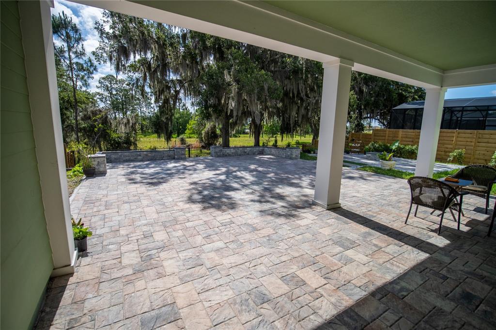 A covered patio features stone pavers, white support columns, and a view of a grassy yard — 6236 TRAILBLAZE BEND, ST CLOUD, FL
