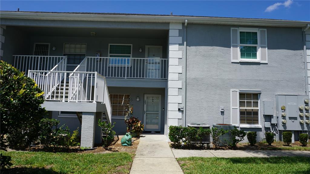 A two-story apartment building exterior features a white staircase, grey stucco walls, and windows — 7713 HILLSIDE COURT UNIT 203, HUDSON, FL