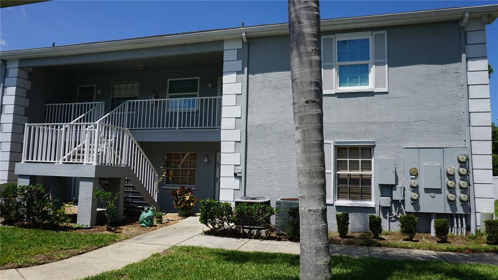 A two-story gray apartment building with white railings, stairs, and exterior utility meters — 7713 HILLSIDE COURT UNIT 203, HUDSON, FL
