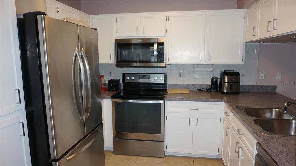 A kitchen features white cabinets, stainless steel appliances, and dark countertops — 7713 HILLSIDE COURT UNIT 203, HUDSON, FL