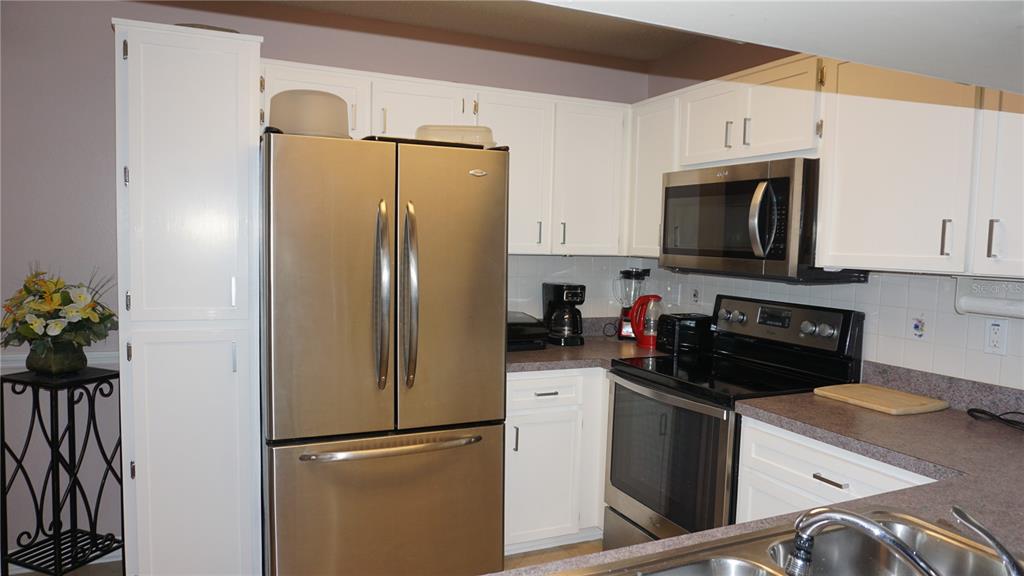 A kitchen features white cabinets, stainless steel appliances, and dark countertops — 7713 HILLSIDE COURT UNIT 203, HUDSON, FL