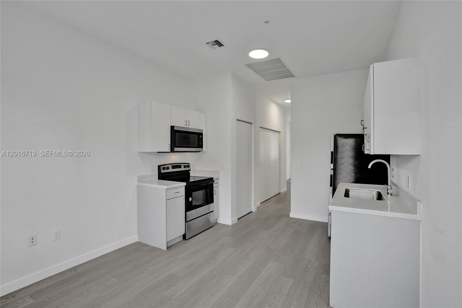 A modern kitchen features white cabinetry, stainless steel appliances, and light wood-look flooring — 1567 NW 1st St # 2, Miami FL 33125, MIAMI, FL