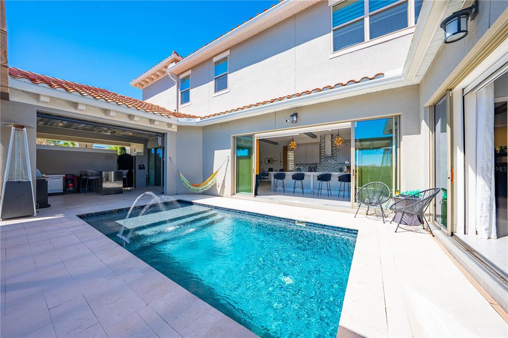 A backyard features a swimming pool with a fountain next to an open-concept indoor kitchen — 9406 MERE PARKWAY, ORLANDO, FL
