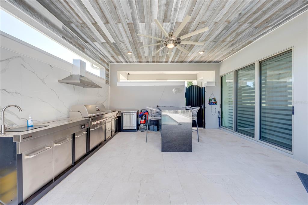 An outdoor kitchen features stainless steel appliances, a stone island, and a wood-paneled ceiling — 9406 MERE PARKWAY, ORLANDO, FL