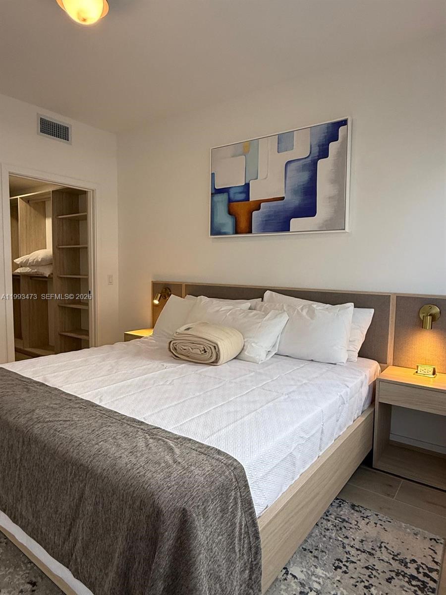 A bedroom features a bed with a gray runner, a headboard with built-in lighting, and a walk-in closet — 225 N Miami Ave # 910, Miami FL 33128, MIAMI, FL
