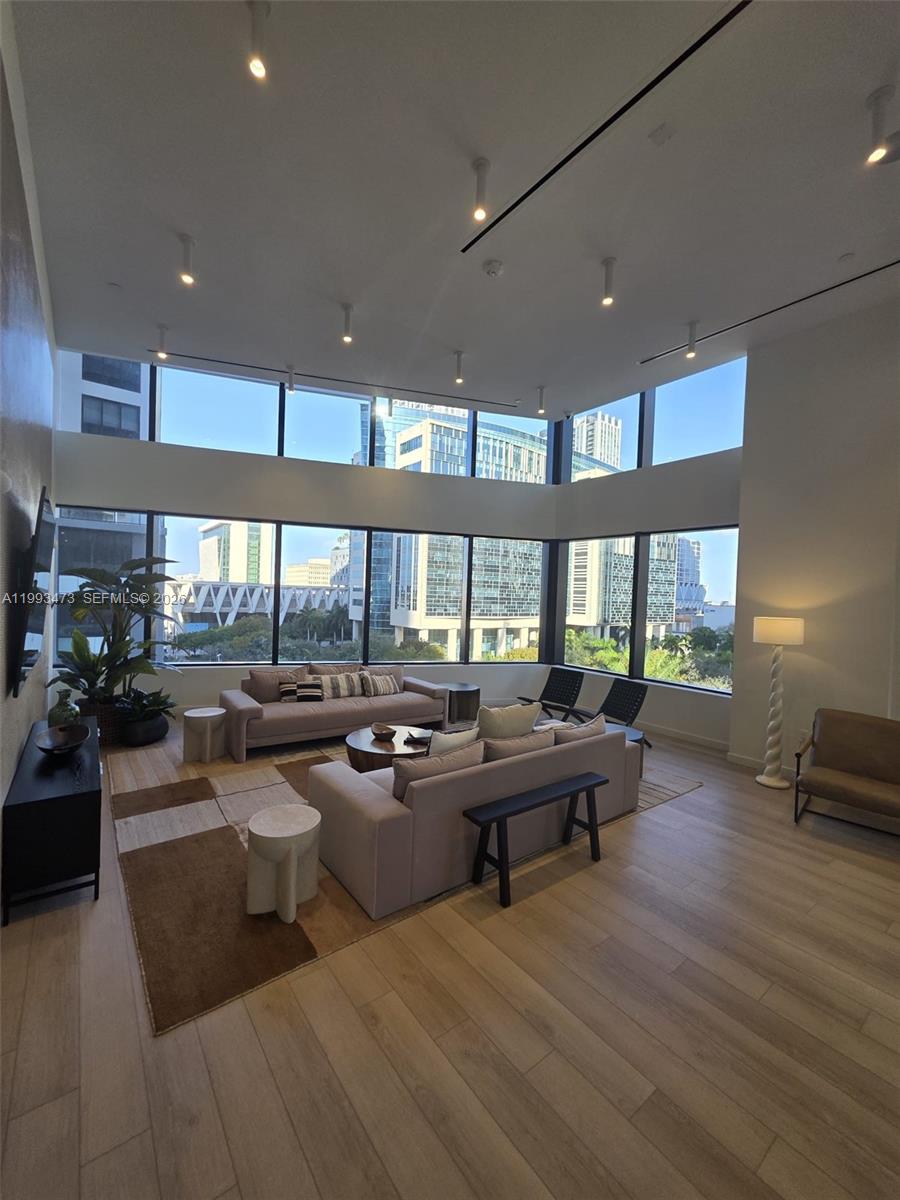 A modern living room features high ceilings, floor-to-ceiling windows, and neutral furniture on hardwood floors — 225 N Miami Ave # 910, Miami FL 33128, MIAMI, FL
