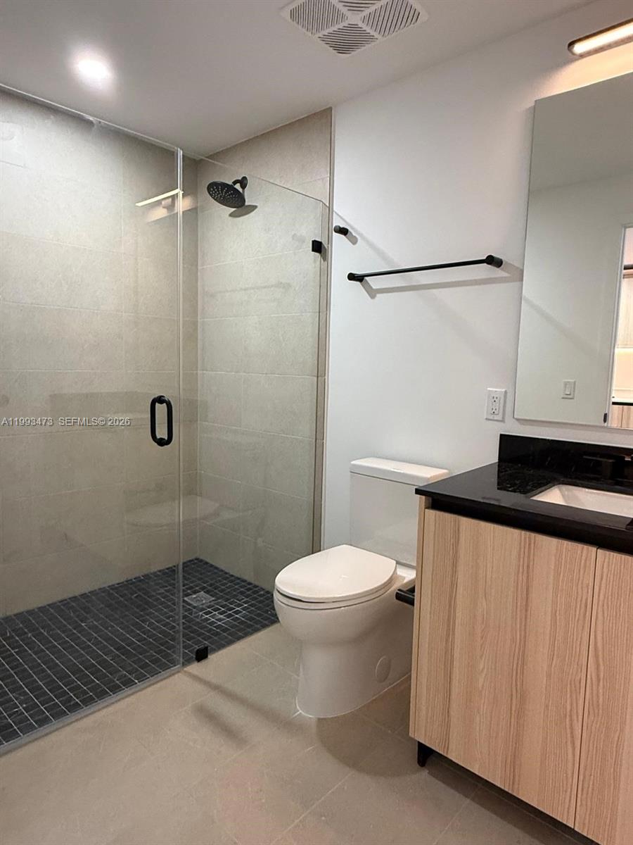 A modern bathroom features a glass-enclosed shower, a toilet, and a wood-toned vanity — 225 N Miami Ave # 910, Miami FL 33128, MIAMI, FL