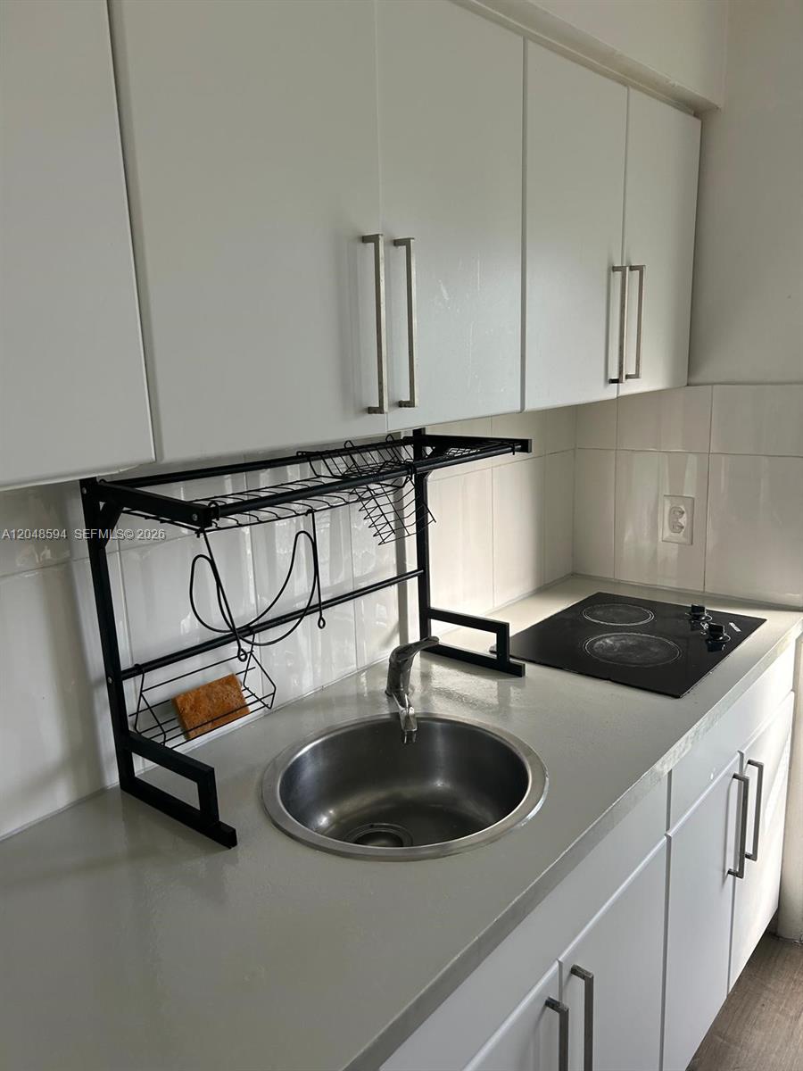 A small kitchen features white cabinets, a stainless steel sink, and a black stovetop — 761 Euclid Ave # 9, Miami Beach FL 33139, MIAMI BEACH, FL