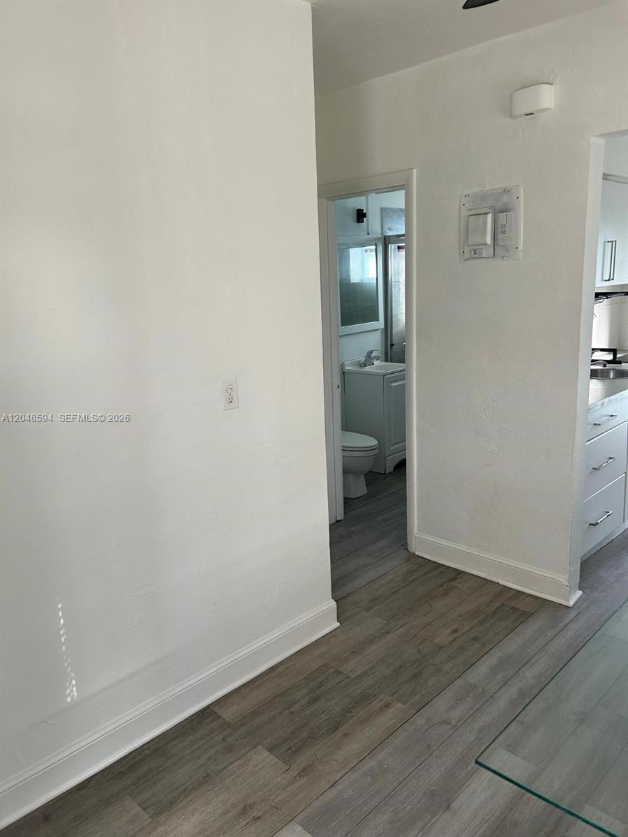A view of a hallway leading to a bathroom with wood-look flooring and white walls — 761 Euclid Ave # 9, Miami Beach FL 33139, MIAMI BEACH, FL