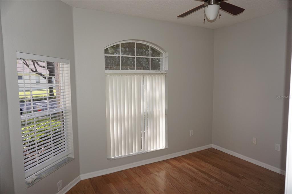 An empty room features hardwood floors, light gray walls, a ceiling fan, and two windows — 19131 CYPRESS REACH LANE, TAMPA, FL